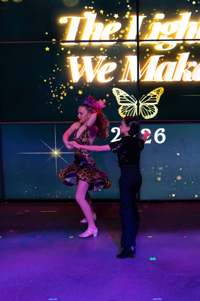 A dancer in a leopard-print latin dress mid-turn with her partner under purple stage light