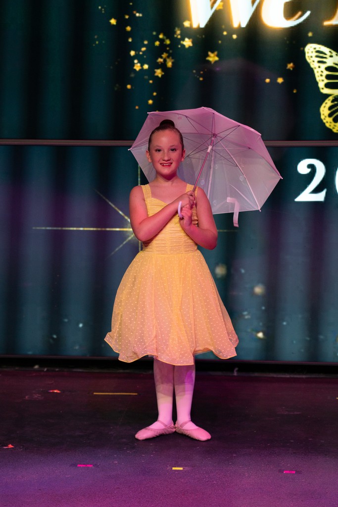 A young dancer performing onstage with a parasol under warm lights