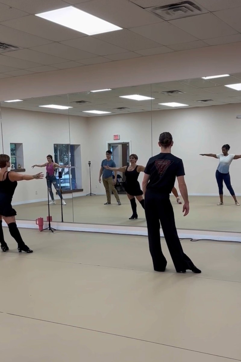 Adult Division dancers working through a combination in class, reflected in the studio mirror