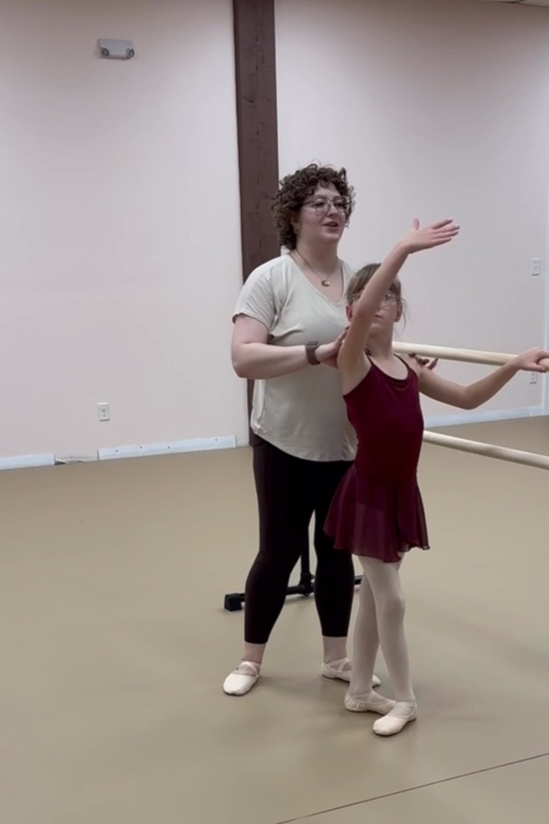 An instructor adjusting a Youth Division dancer’s arm at the barre